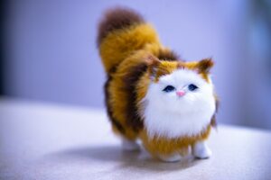 Here's a caption: fluffy, adorable stuffed cat looking directly at viewer.